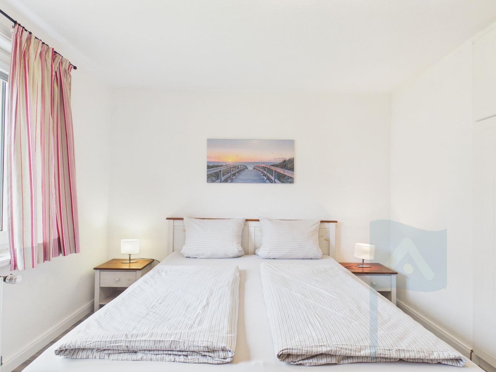 Zimmer mit Doppelbett, zwei Nachttischen und Wandbild. Vorhang mit Streifen.