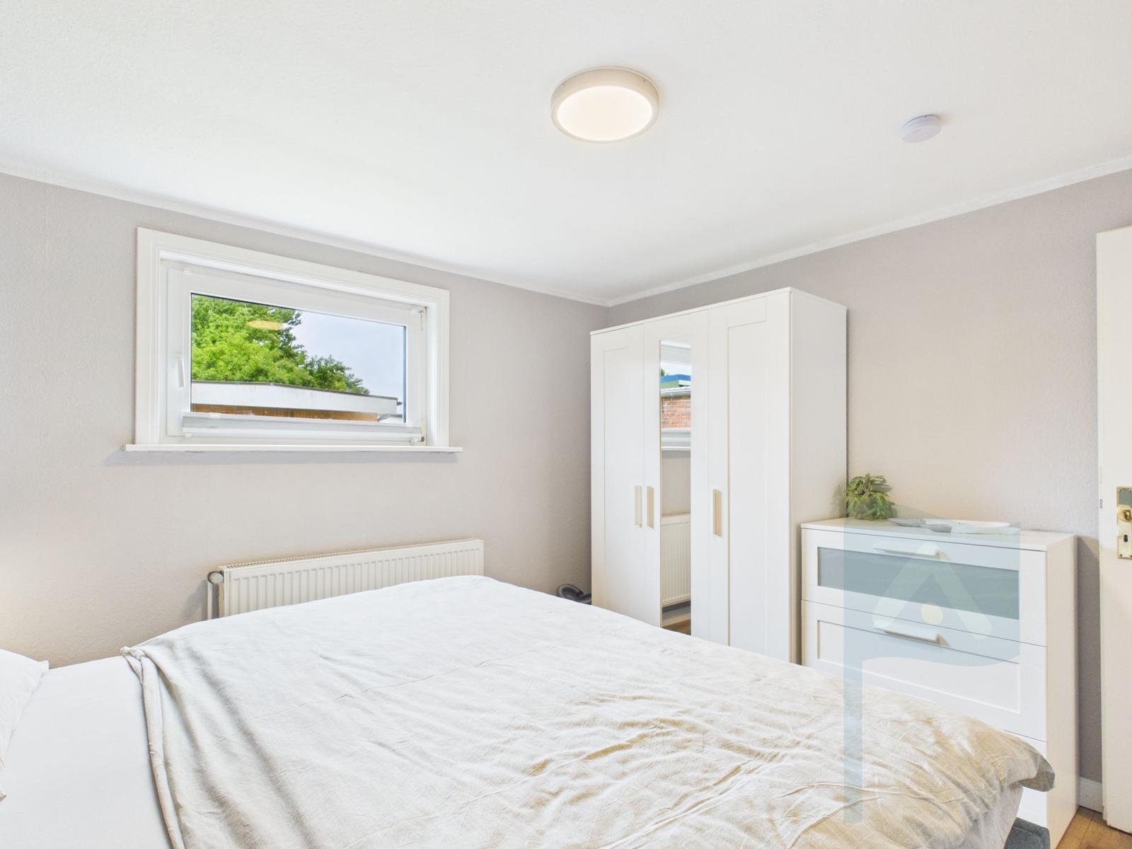 Schlafzimmer mit Bett, Kleiderschrank und Fenster zum Garten.