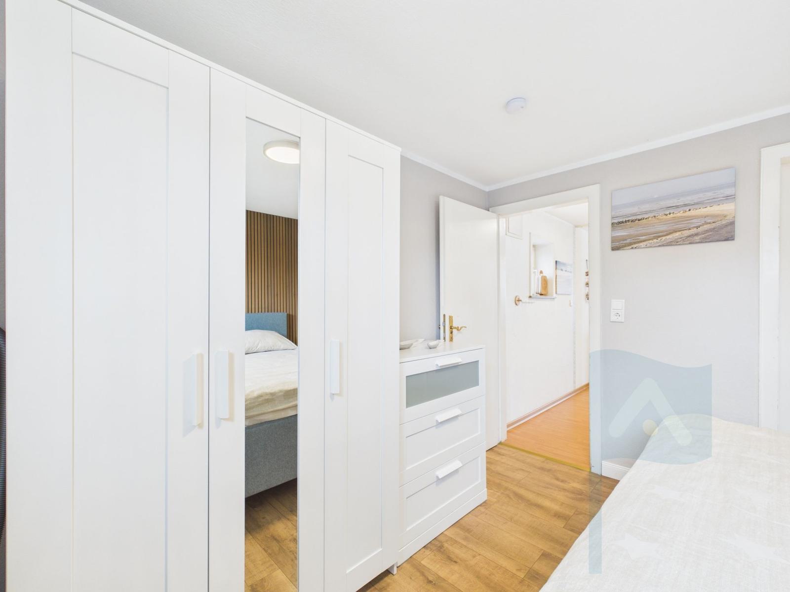 Schlafzimmer mit weißem Schrank und Bett. Holzboden und Wandbild.