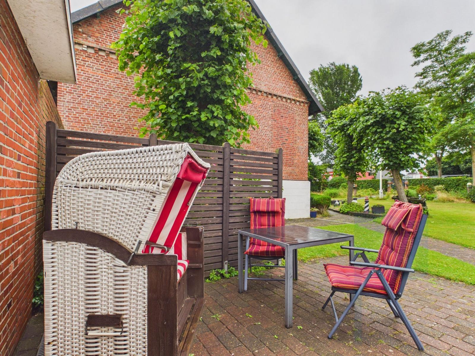 Terrasse mit Stuhl, Tisch und Liegestuhl vor Backsteinhaus mit Grünflächen.