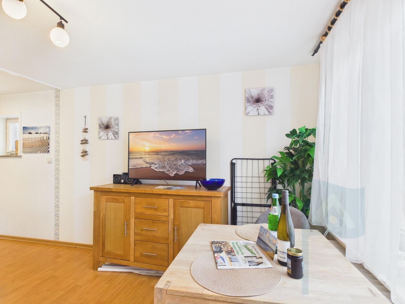Ein Wohnzimmer mit Holzmöbeln, Fernseher und Pflanze. Tisch mit Zeitung und Flaschen.