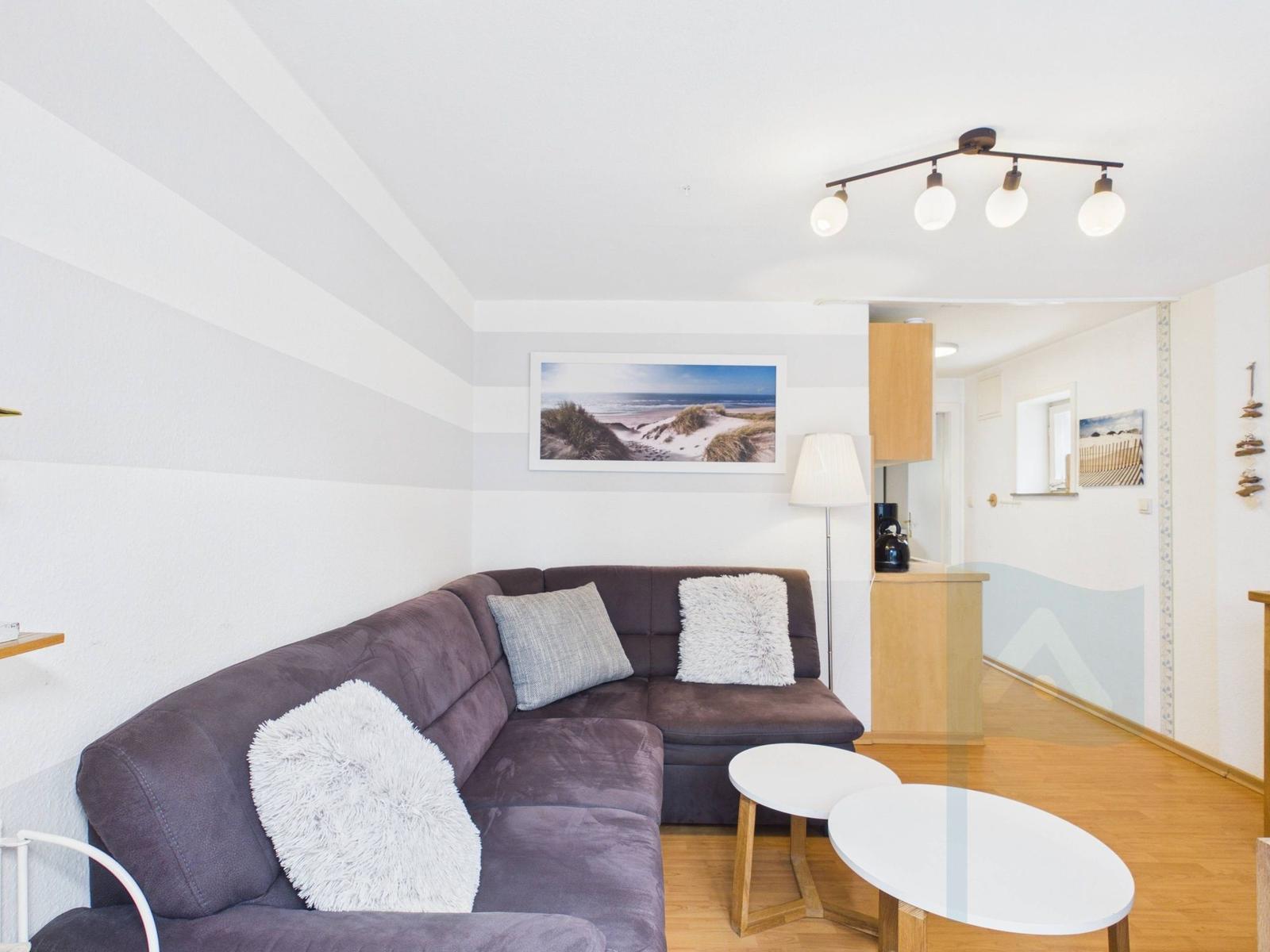 Ein Wohnzimmer mit einem grauen Sofa, zwei weißen Kissen und zwei runden Tischen.