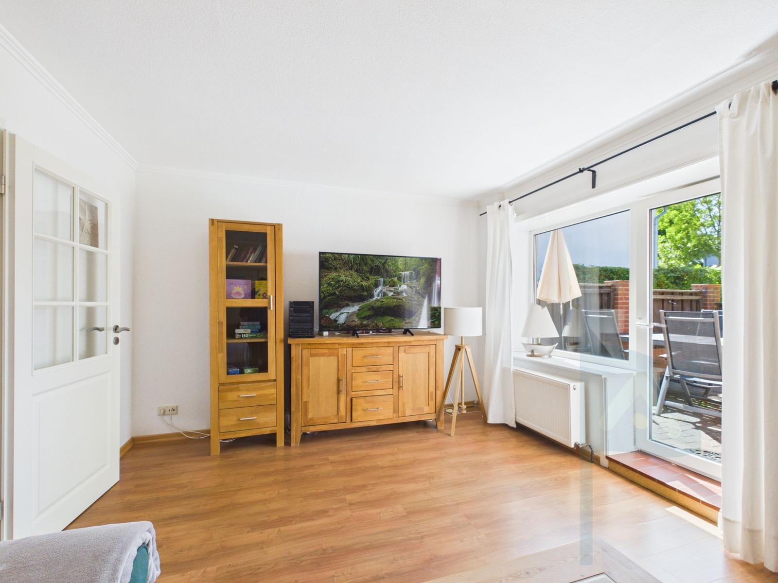 Living room with wooden furniture, TV, and view of the terrace.