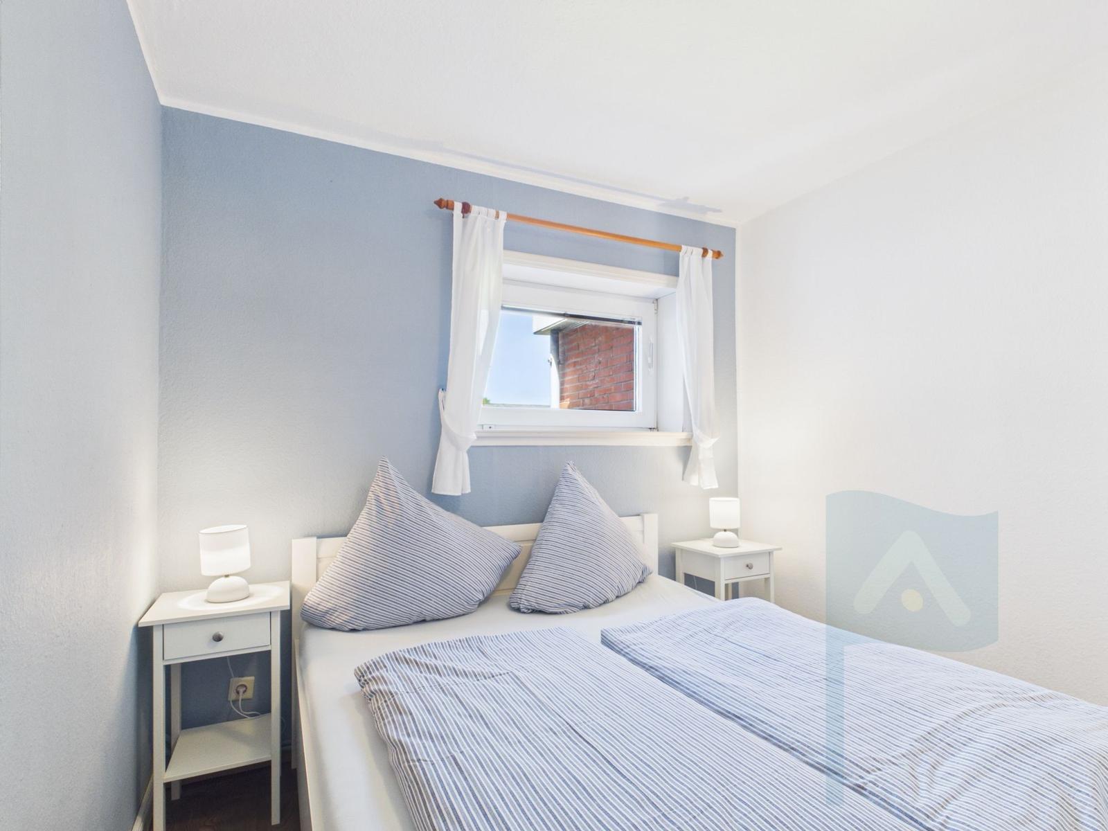 Bedroom with bed, two nightstands, and window with white curtains.
