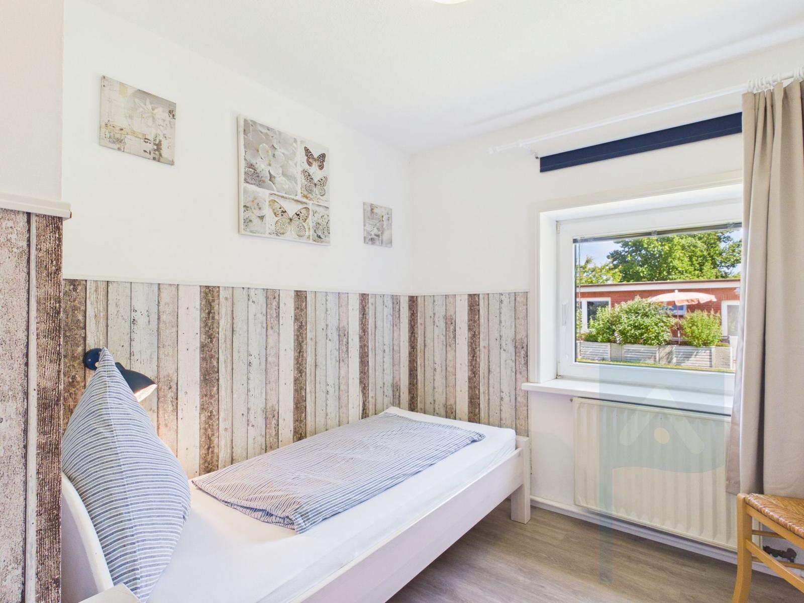 A bedroom with a bed, wooden wall, and window overlooking the garden.