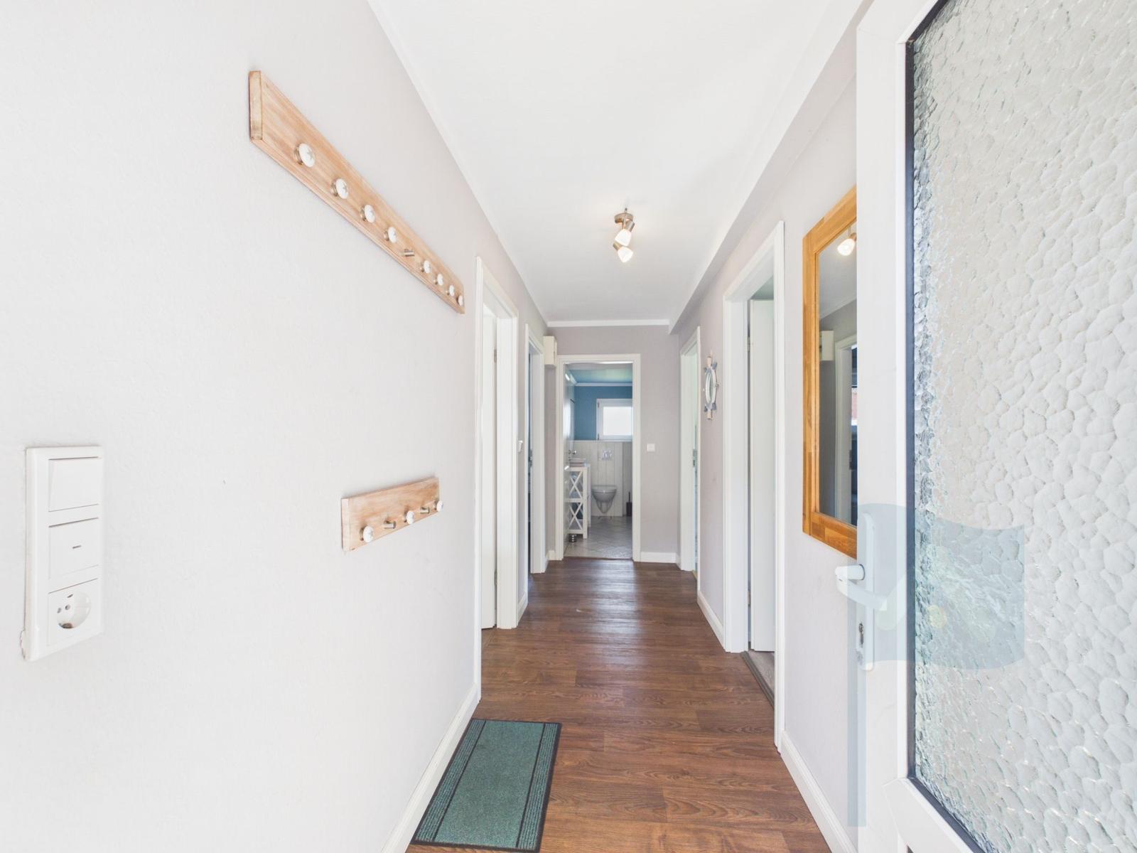Hallway with wooden floor, coat rack, and door to the bathroom.