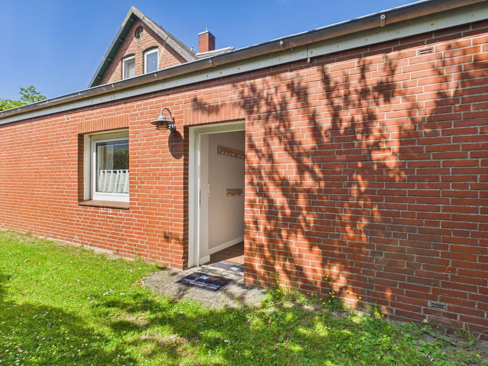 Red brick house with entrance and window. Grass area in front of the wall.