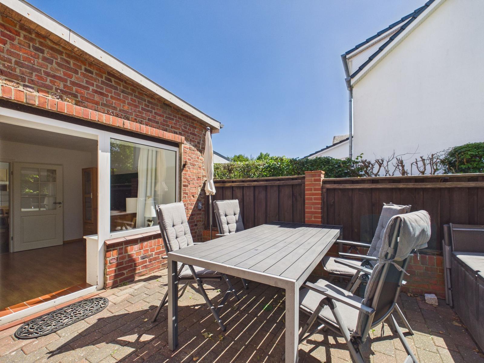 Terrace with table and chairs, adjacent to a house with brick facade.