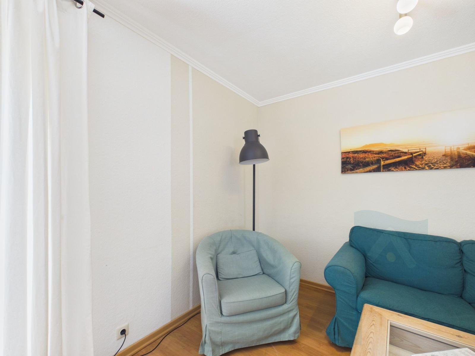 A room with a light blue armchair, a teal sofa, and wall decor.