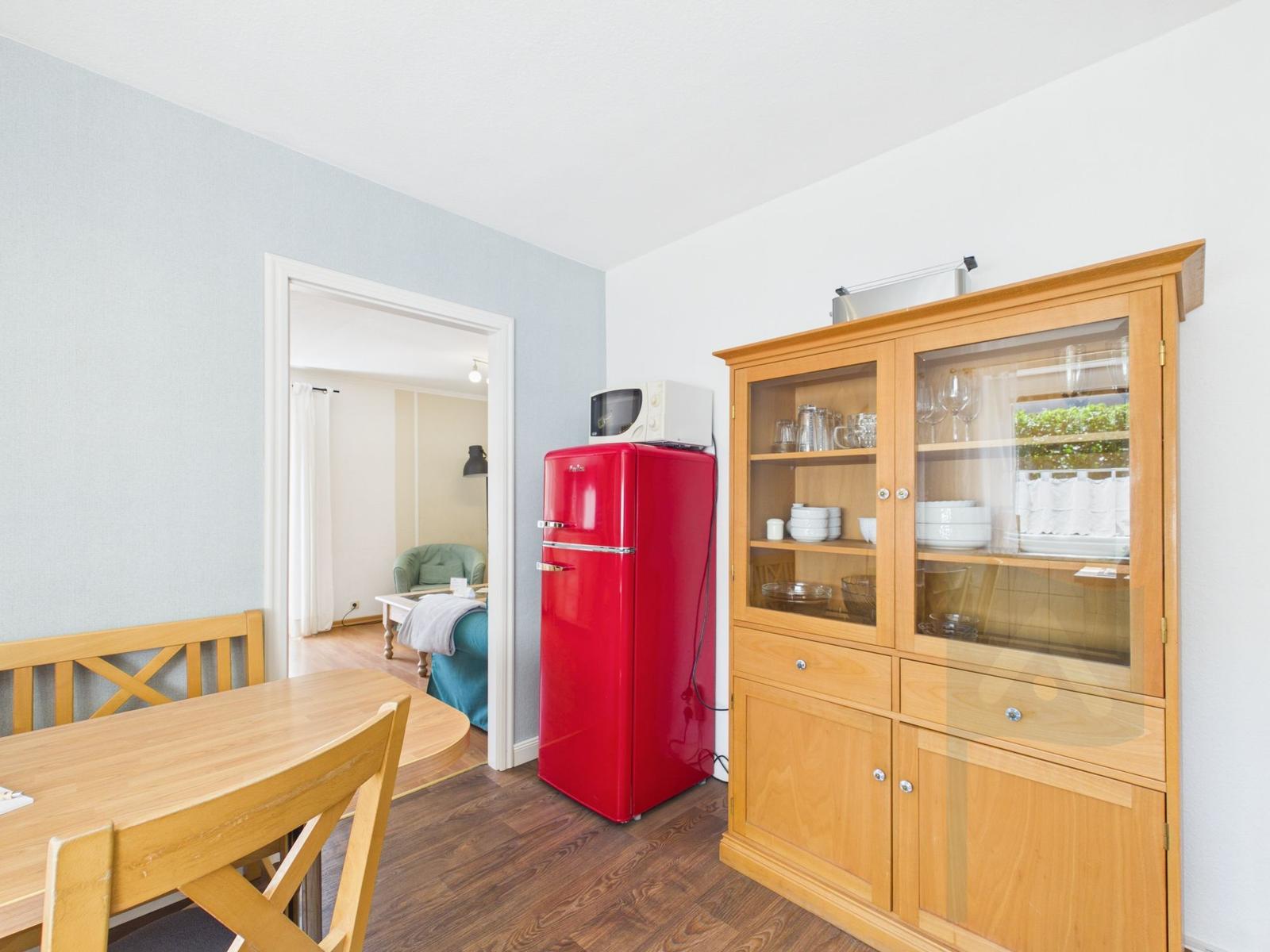 Dining area with wooden table, red refrigerator, and wooden cabinet with dishes.