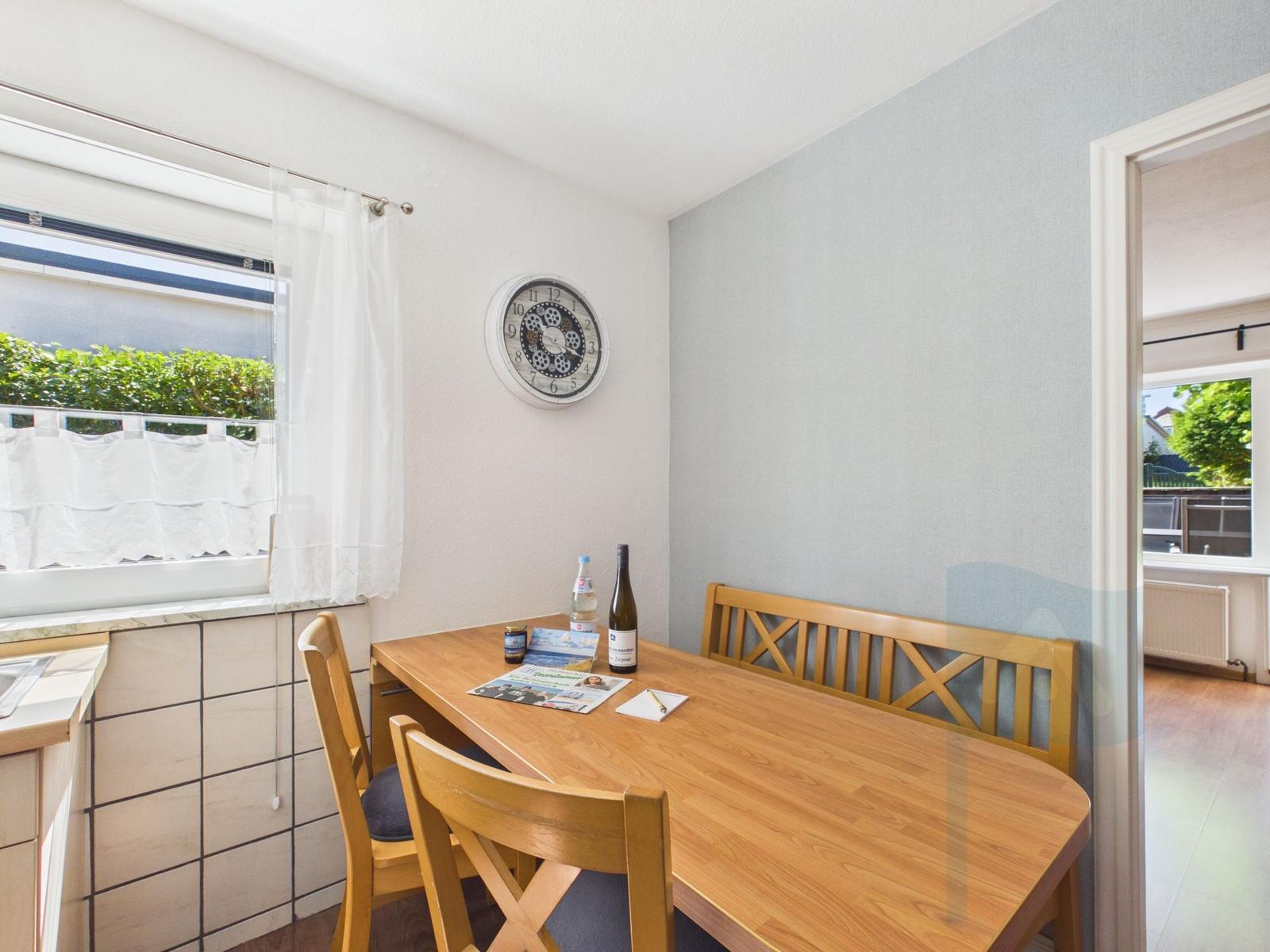 Dining room with wooden table, chairs, and wall clock. Window with curtain. Door to hallway.