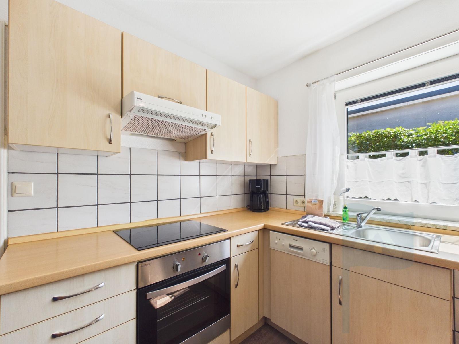 Kitchen with wooden cabinets, stove, sink, and window.