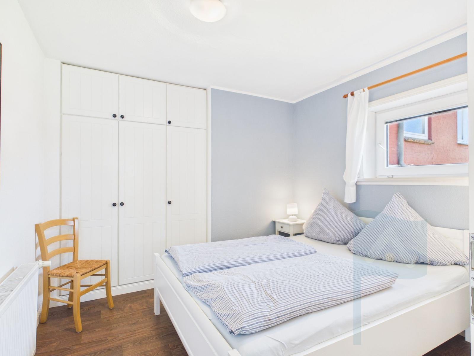 Bedroom with white bed, wardrobe, and window.