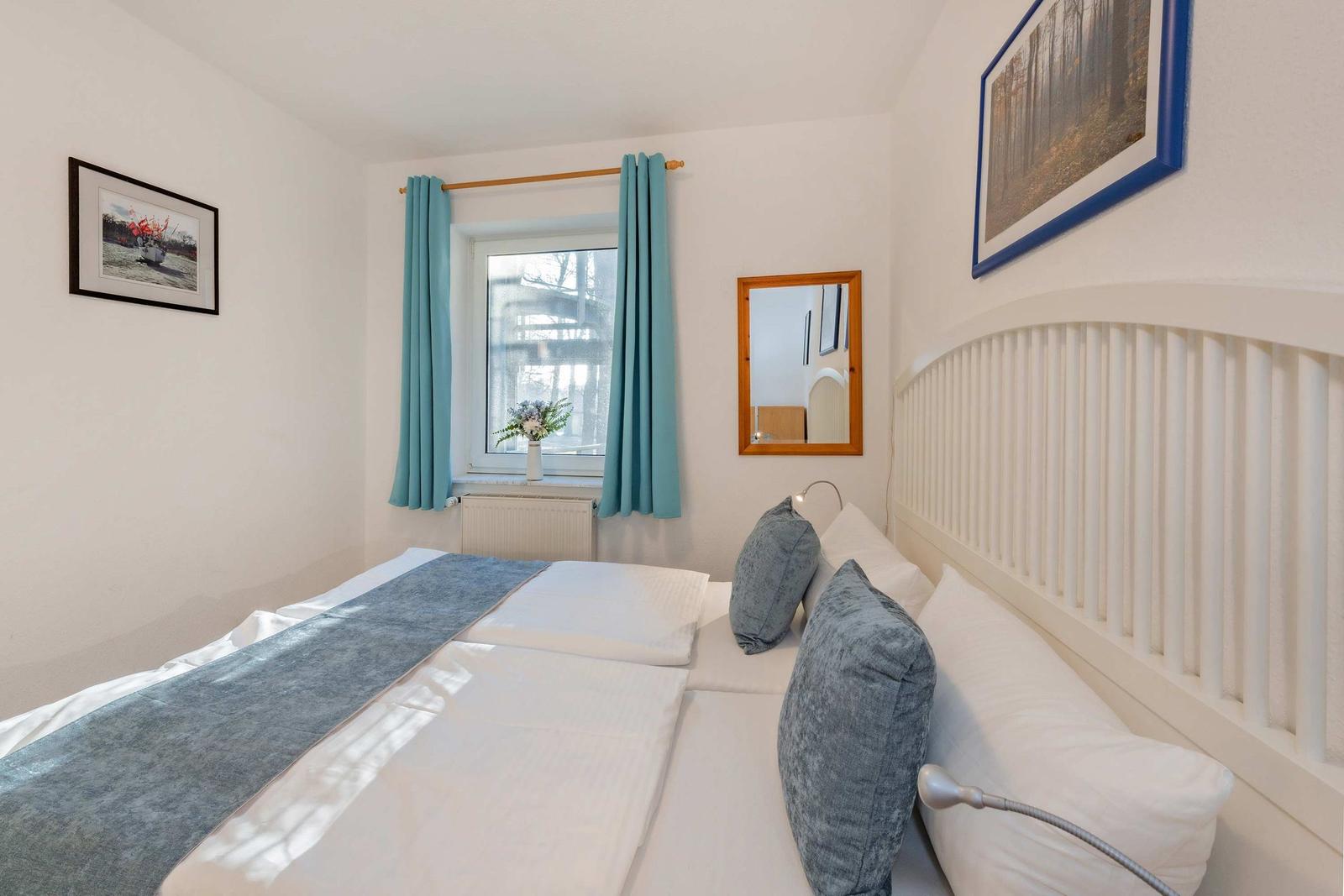 Schlafzimmer mit Bett, Fenster, Vorhängen und Wandbildern.