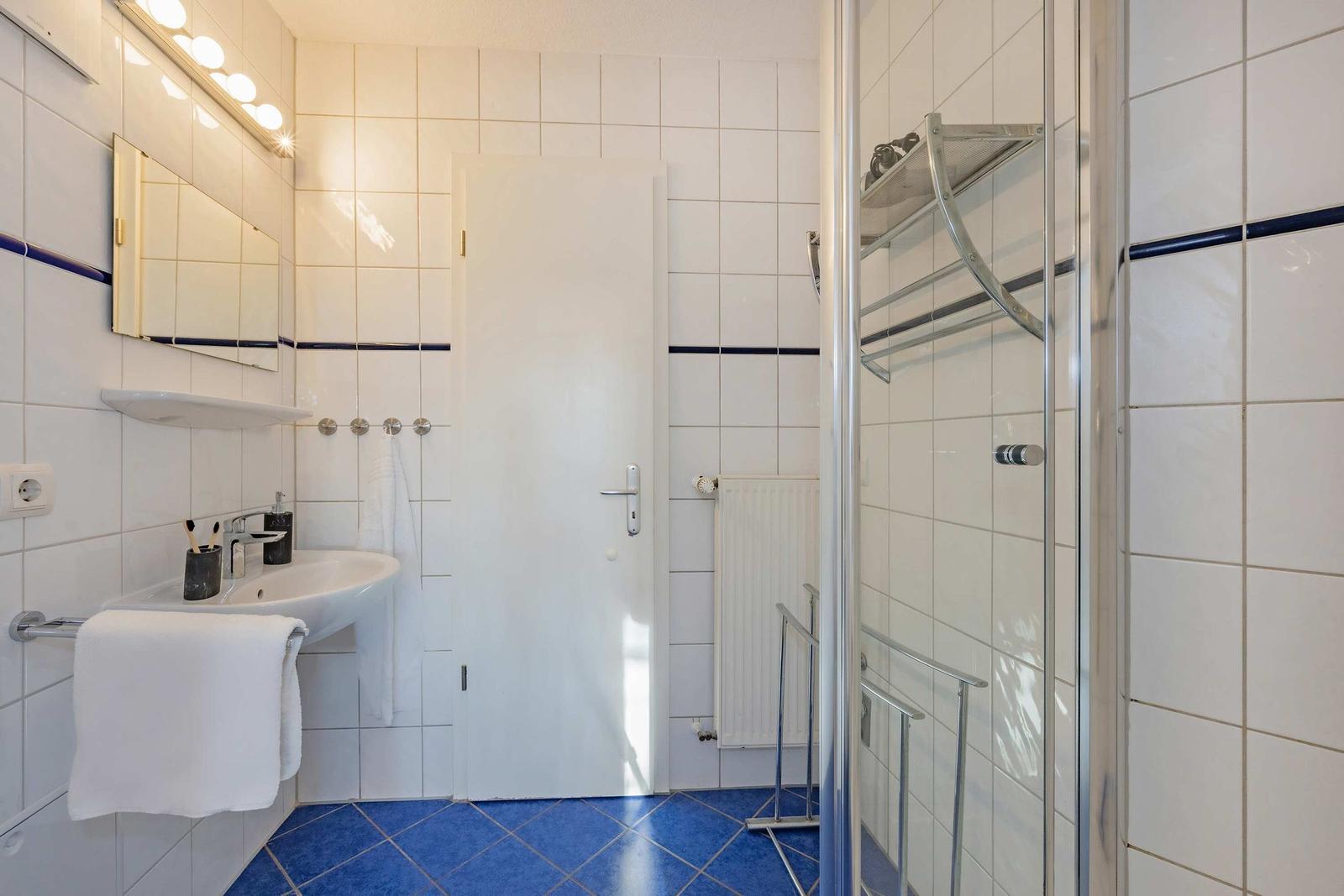 Badezimmer mit Dusche, Waschbecken und Spiegel. Fliesenboden und weiße Wände.