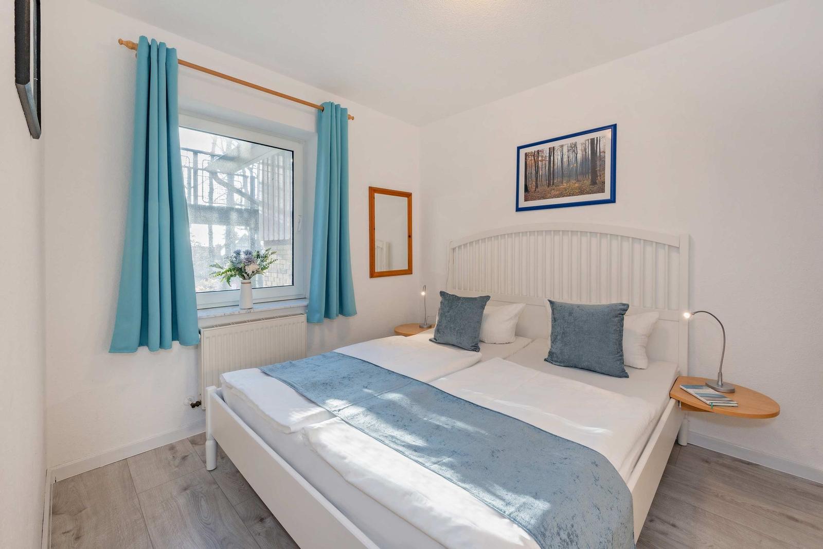 Schlafzimmer mit Doppelbett, blauen Vorhängen und Wandbild.