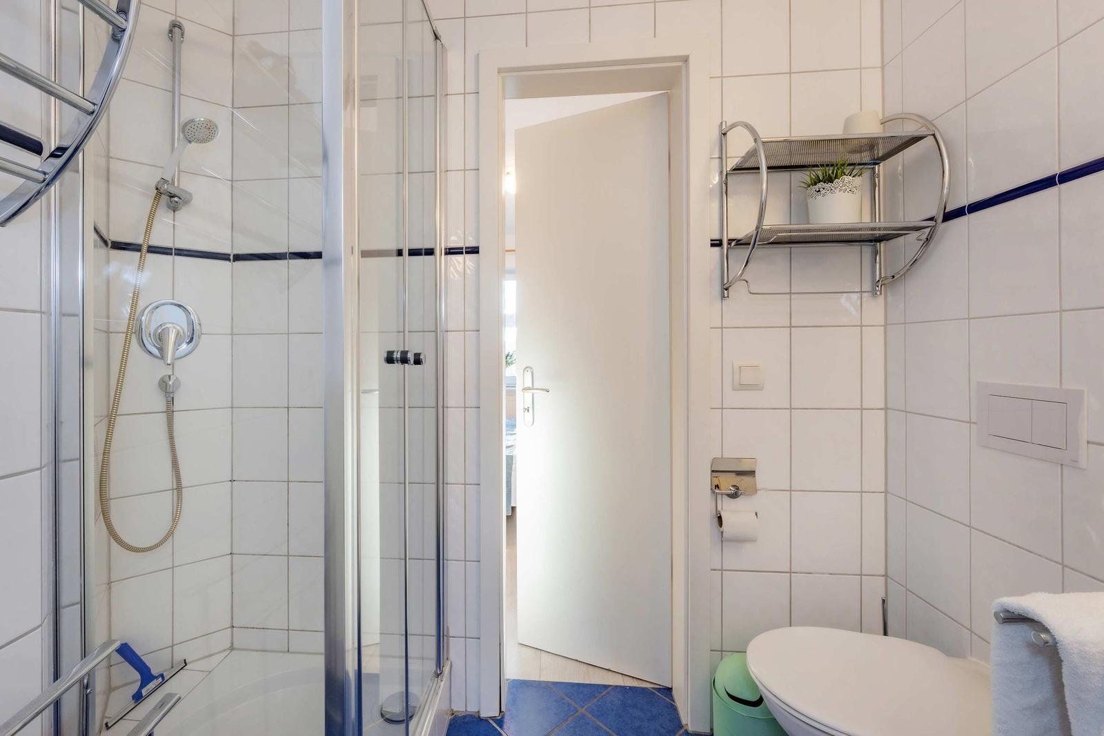 Badezimmer mit Dusche, Toilette und Handtuchhalter. Weiße Fliesen und blaue Bodenfliesen.