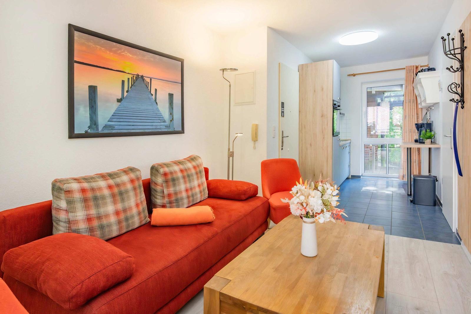 Wohnbereich mit rotem Sofa, Holztisch und Küchenbereich im Hintergrund.