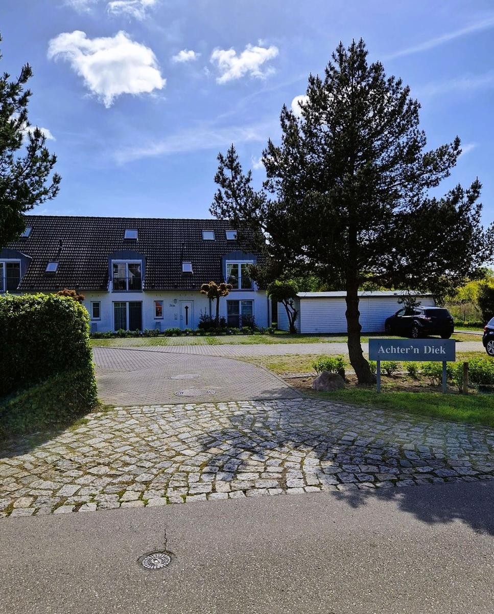 Haus mit Kiesweg und Schild Achtern Diek unter blauem Himmel.