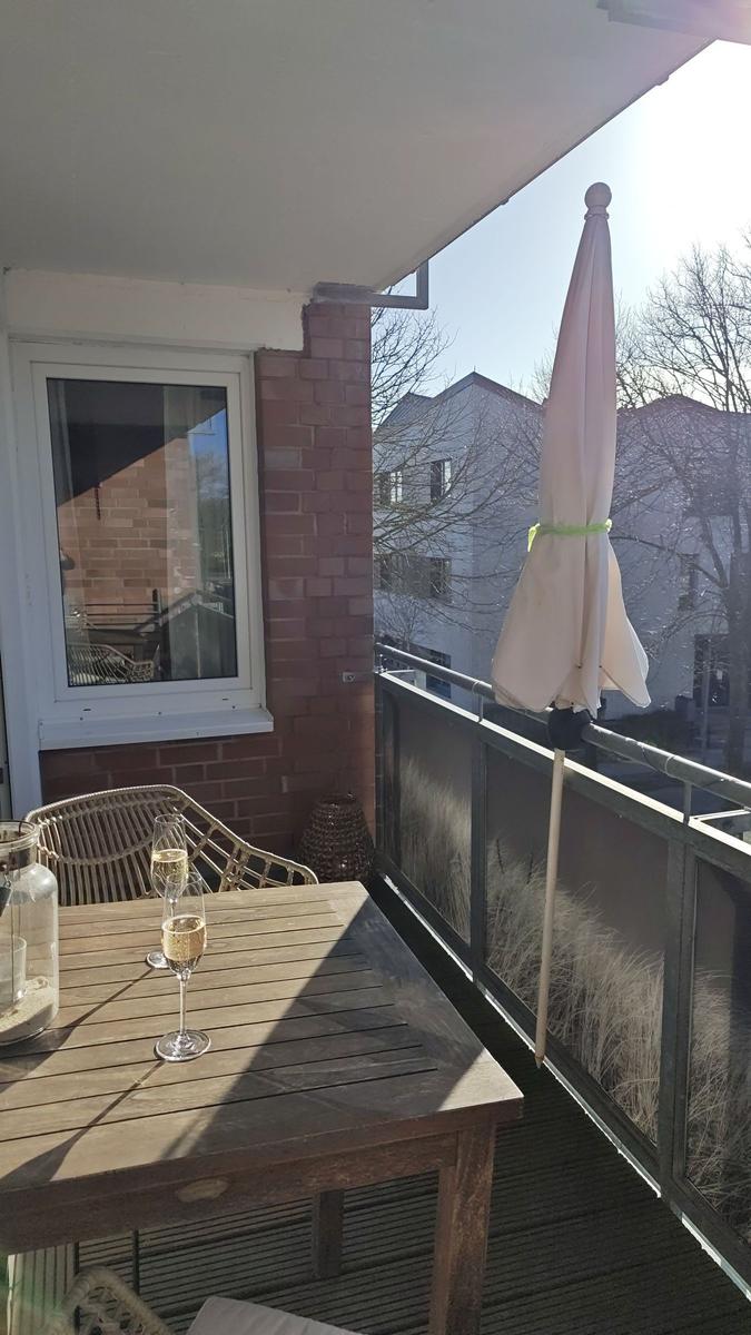 Terrasse mit Tisch, Stühlen und geschlossenem Sonnenschirm. Hintergrund: Gebäude und kahle Bäume.