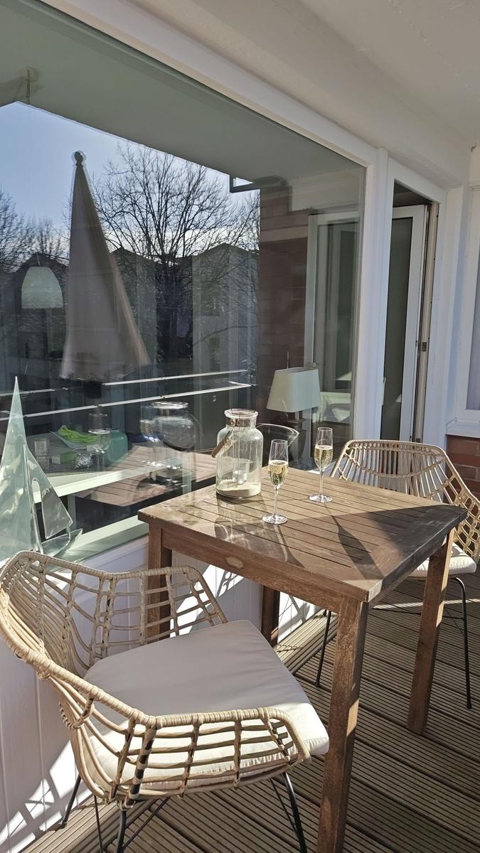 Terrasse mit Holztisch, zwei Stühlen und zwei Gläsern mit Getränk.