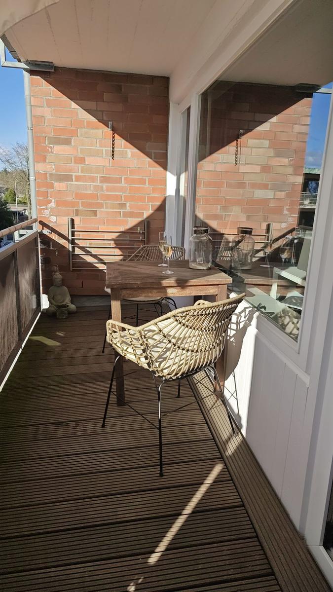 Terrasse mit Holztisch, Stühlen und Buddha-Statue. Holzdielenboden und Backsteinmauer im Hintergrund.