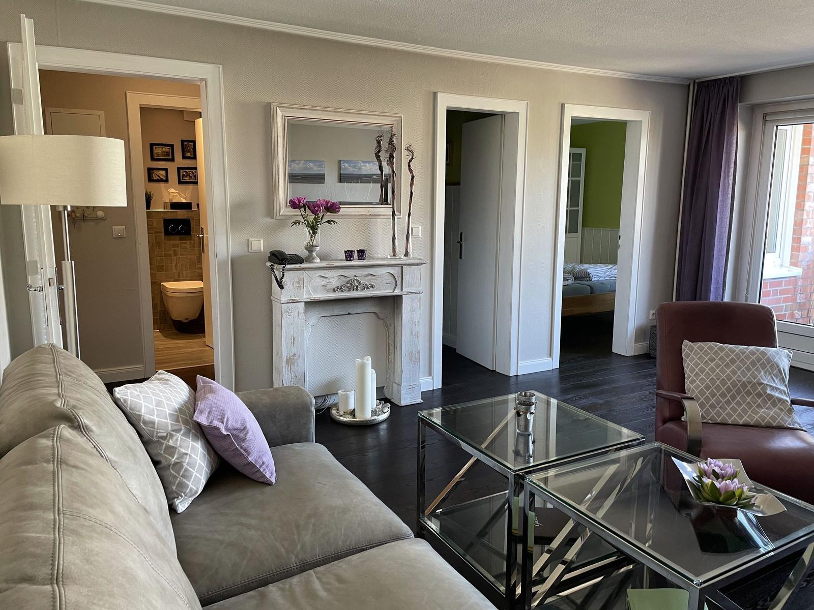 Wohnzimmer mit Sofa, Glas-Tisch und Kamin. Blick in Schlaf- und Badezimmer.