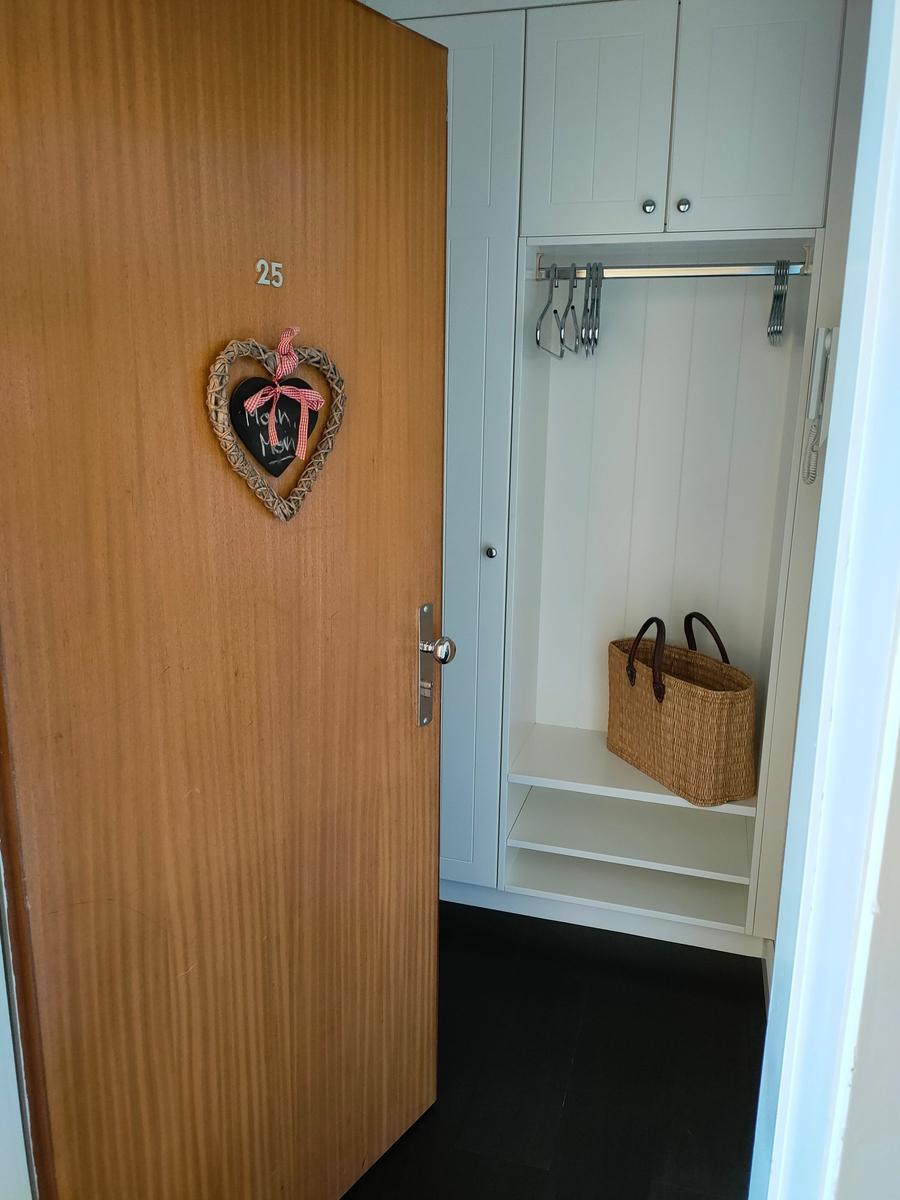 Tür mit Herzdekoration führt zu einem weißen Kleiderschrank mit Ablage und Haken.