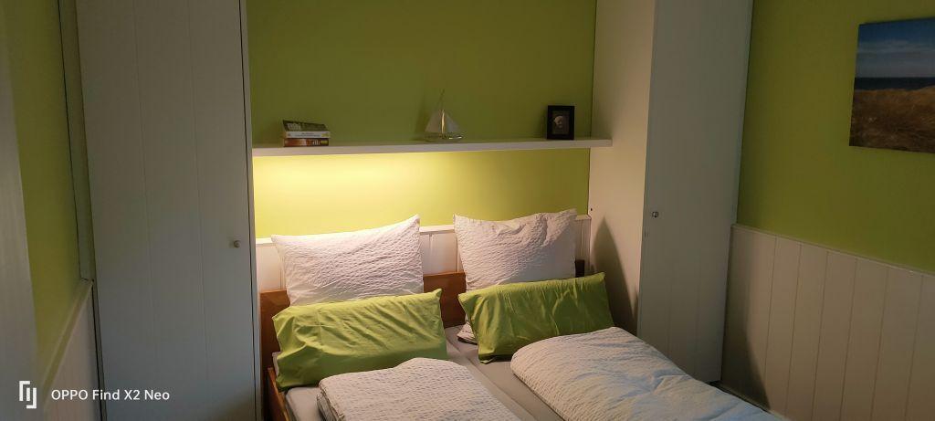 Zimmer mit zwei Betten, grüner Wand und Regal mit Dekoration.
