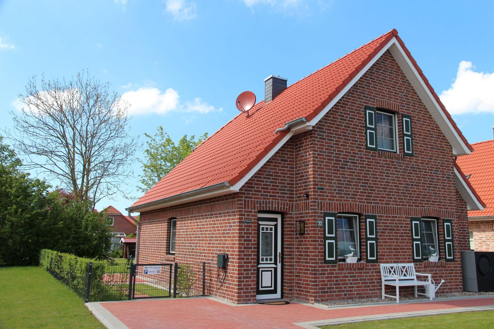 Rotes Dach, Backsteinhaus mit weißen Fensterläden und einer weißen Bank vor dem Eingang.