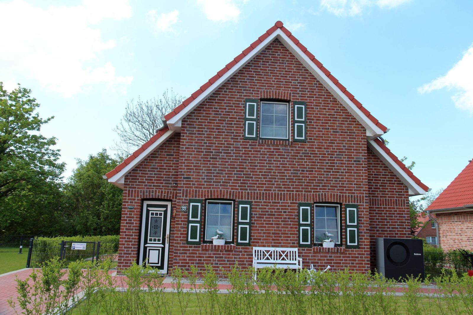 Ein rotes Backsteinhaus mit weißer Veranda und grünen Fensterläden.
