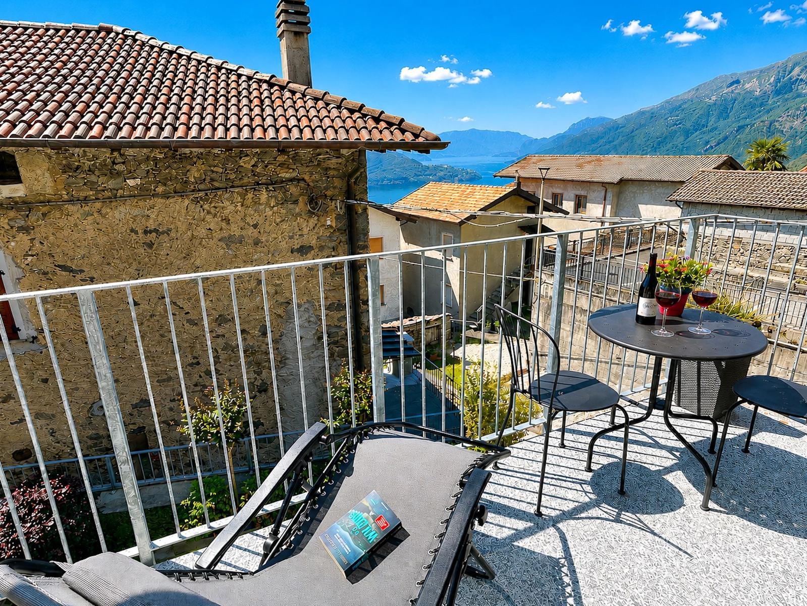 Terrasse mit Tisch, Stühlen und Liegestuhl. Blick auf See und Berge.