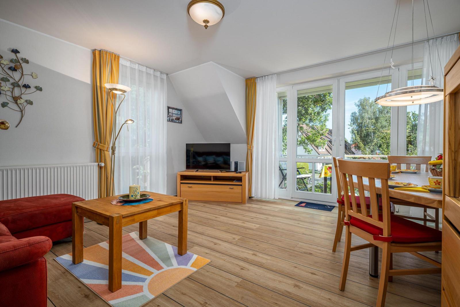 Wohn- und Essbereich mit Holzboden, TV, Tisch und Stühlen sowie Balkontür.