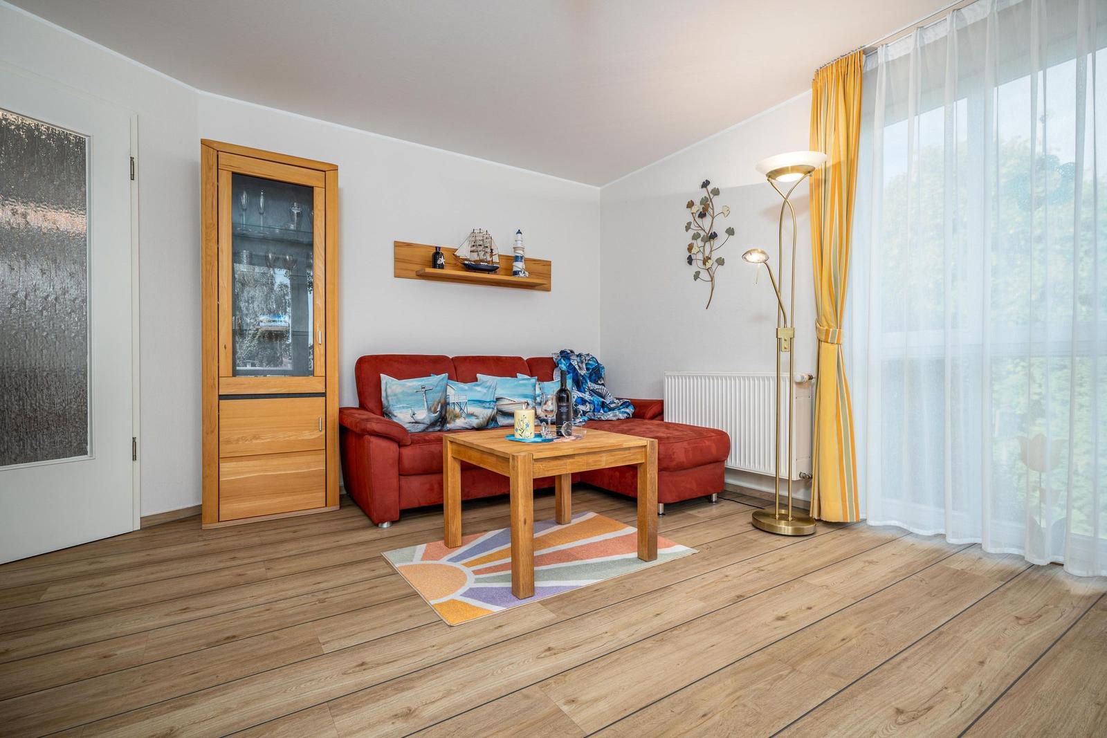 Ein Wohnzimmer mit rotem Sofa, Holztisch und großen Fenstern mit gelben Vorhängen.