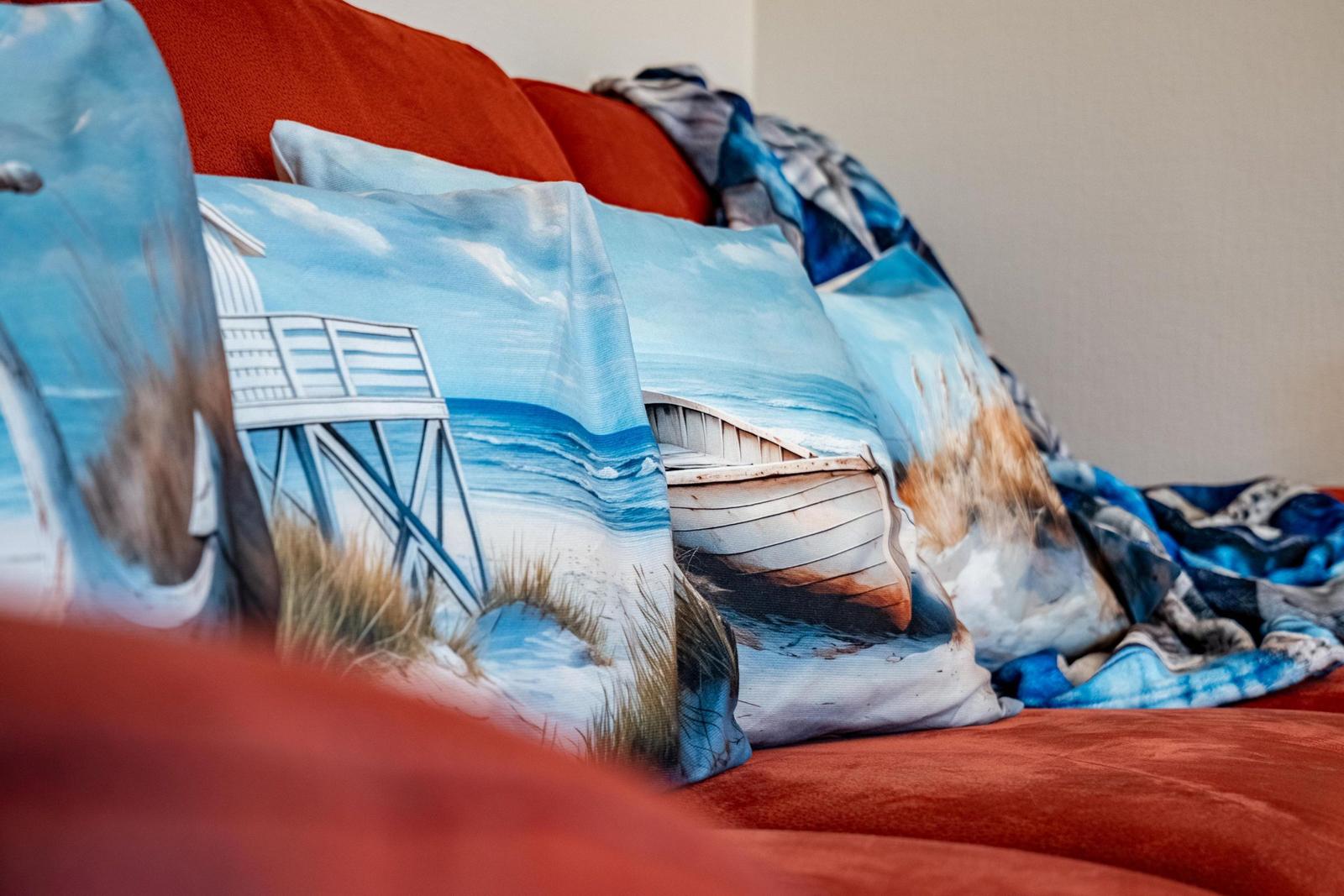 Rote Couch mit Kissen und Decke mit Strandmotiv.
