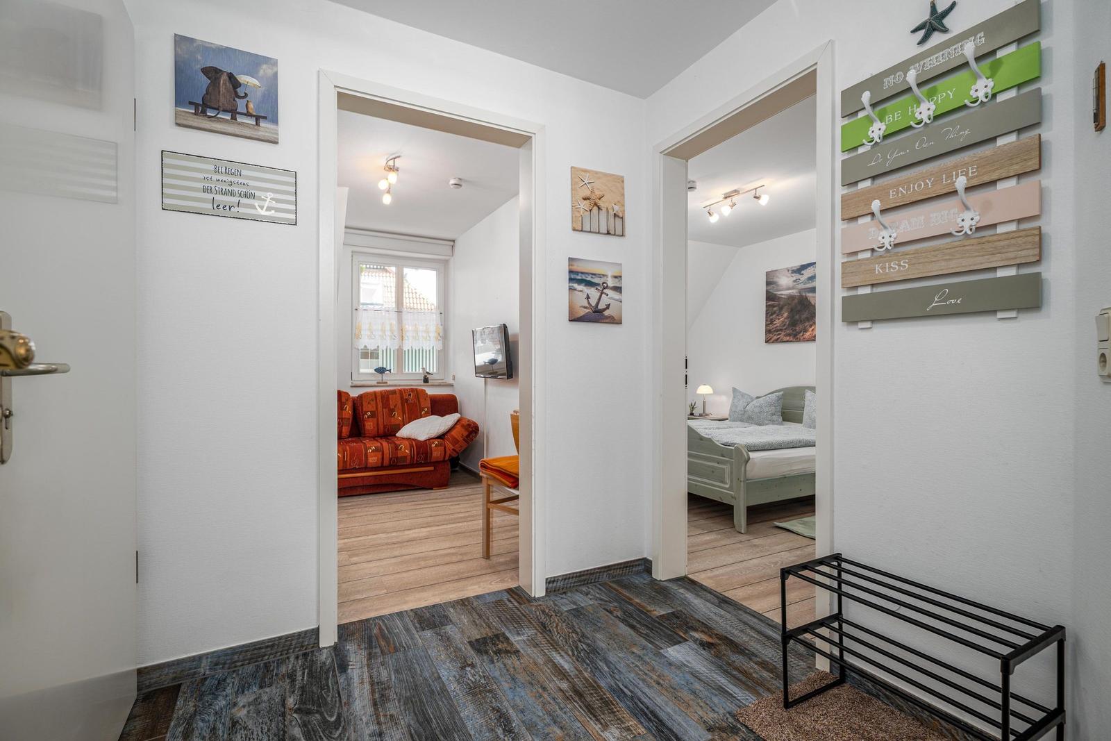 Eingangsbereich mit Blick in Wohn- und Schlafzimmer. Wanddekoration und Holzboden sichtbar.