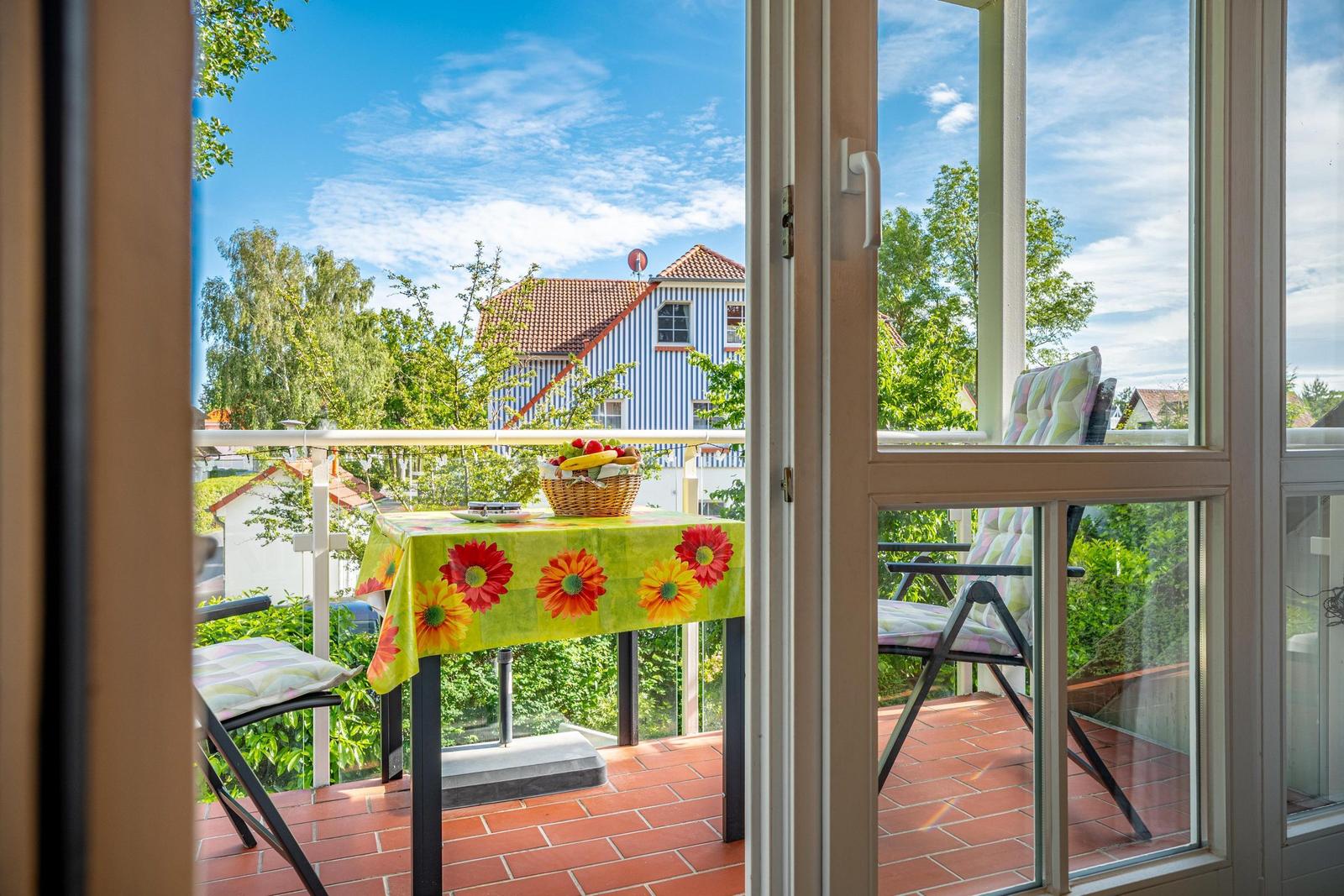 Balkon mit Tisch, Stühlen und Blick auf ein Haus mit rotem Dach.