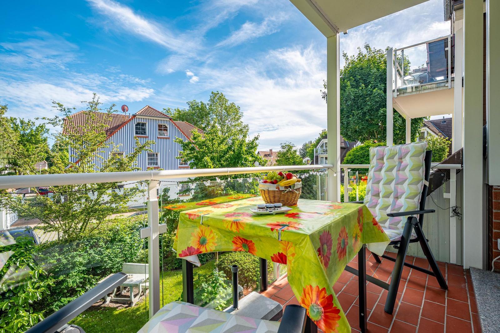 Terrasse mit Tisch, Stühlen und Obstkorb. Blick auf grüne Bäume und ein Haus.