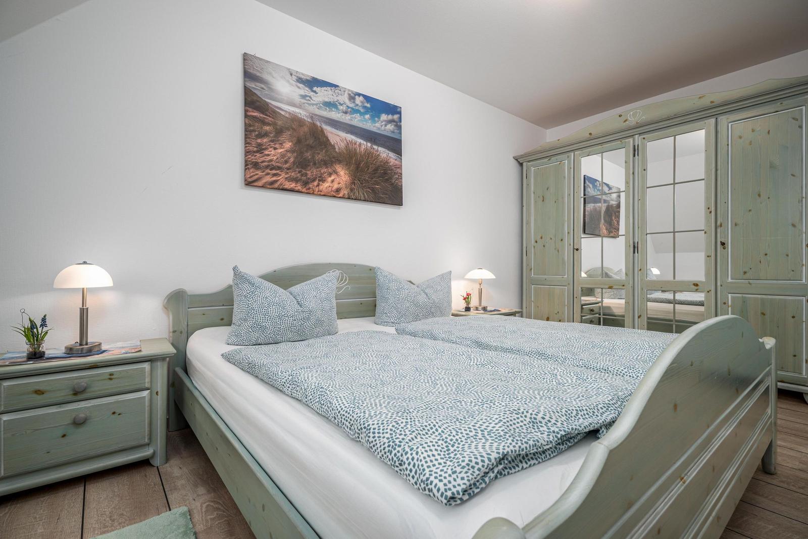Schlafzimmer mit Bett, Nachttisch und Kleiderschrank. Wandbild zeigt Strand.