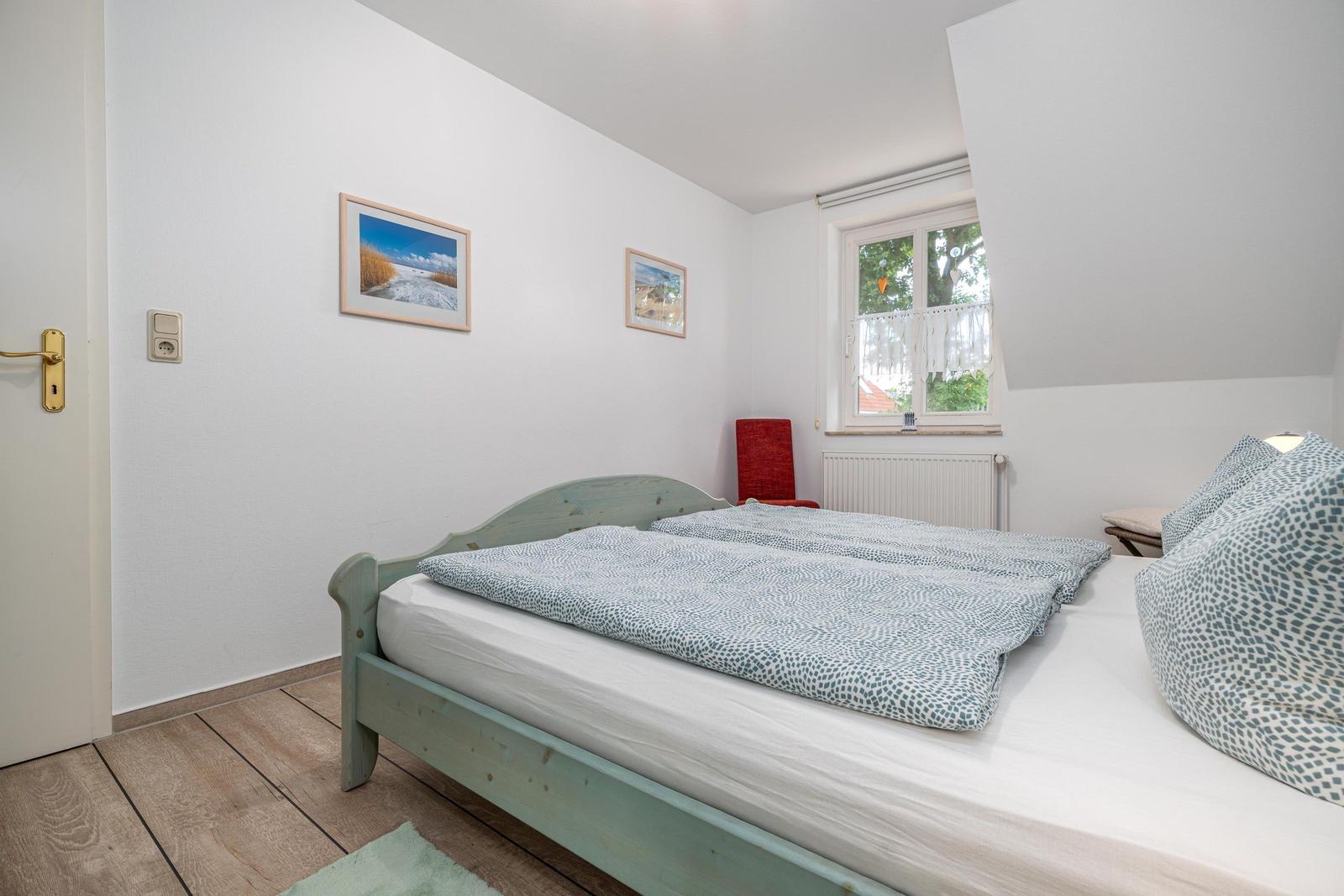 Schlafzimmer mit Bett, Fenster und Wandbildern.