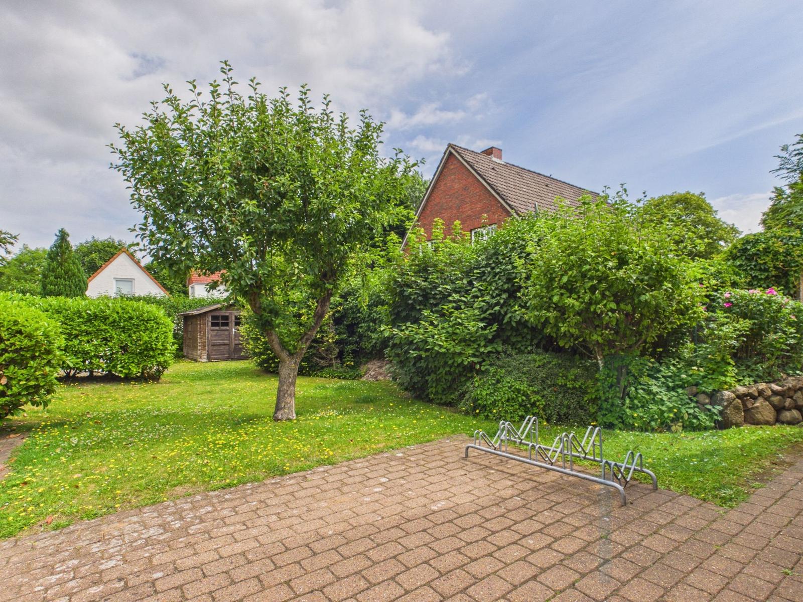 Haus mit Garten, Baum und Fahrradständer. Grasfläche mit Blumen.