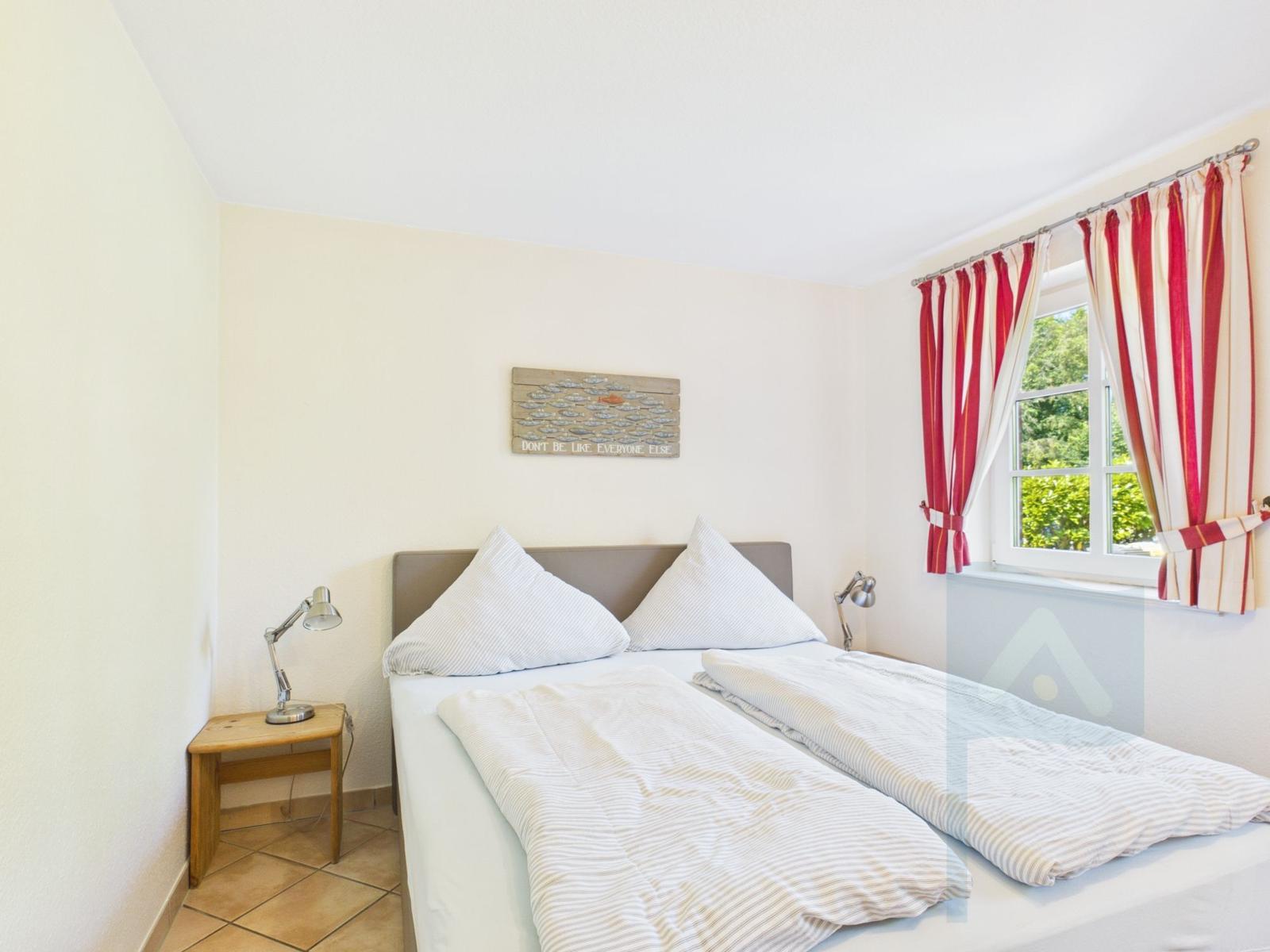 Ein Schlafzimmer mit Bett, Nachttisch und Fenster mit roten Vorhängen.