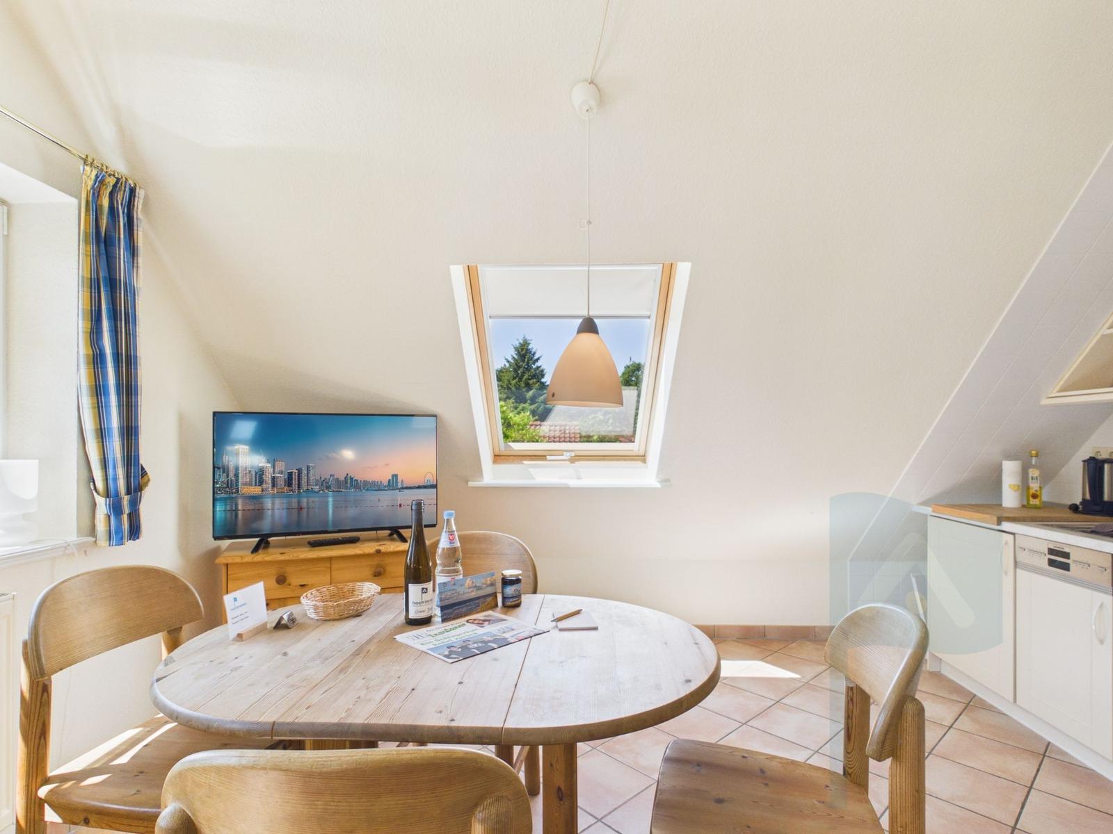 Rundtisch mit Stühlen, TV und Fenster mit Blick auf Grün.