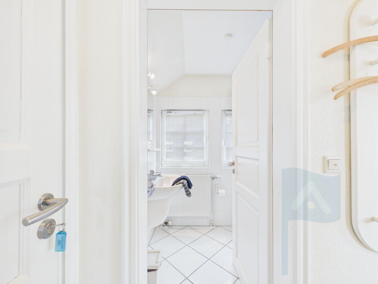 Badezimmer mit Waschbecken, Heizkörper und Fenster mit Jalousie.