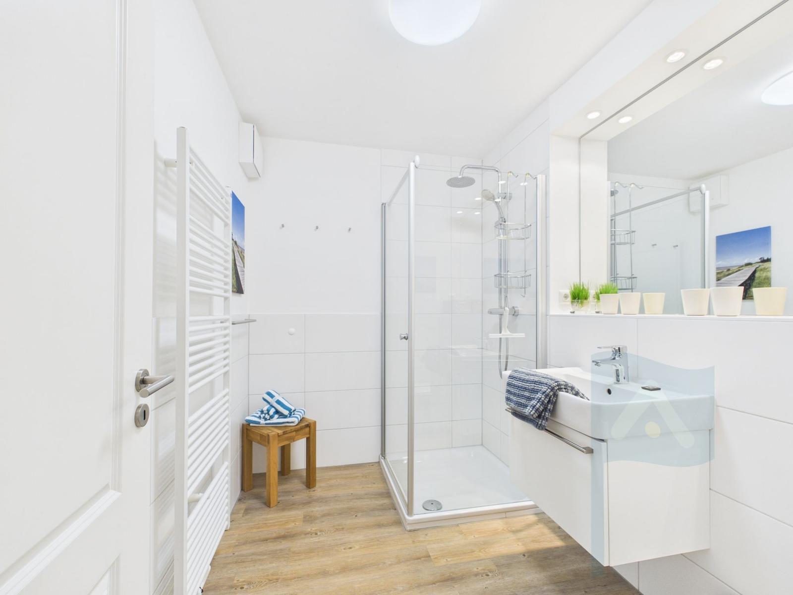 Badezimmer mit Dusche, Waschbecken und Heizung. Holzfußboden und Spiegel.