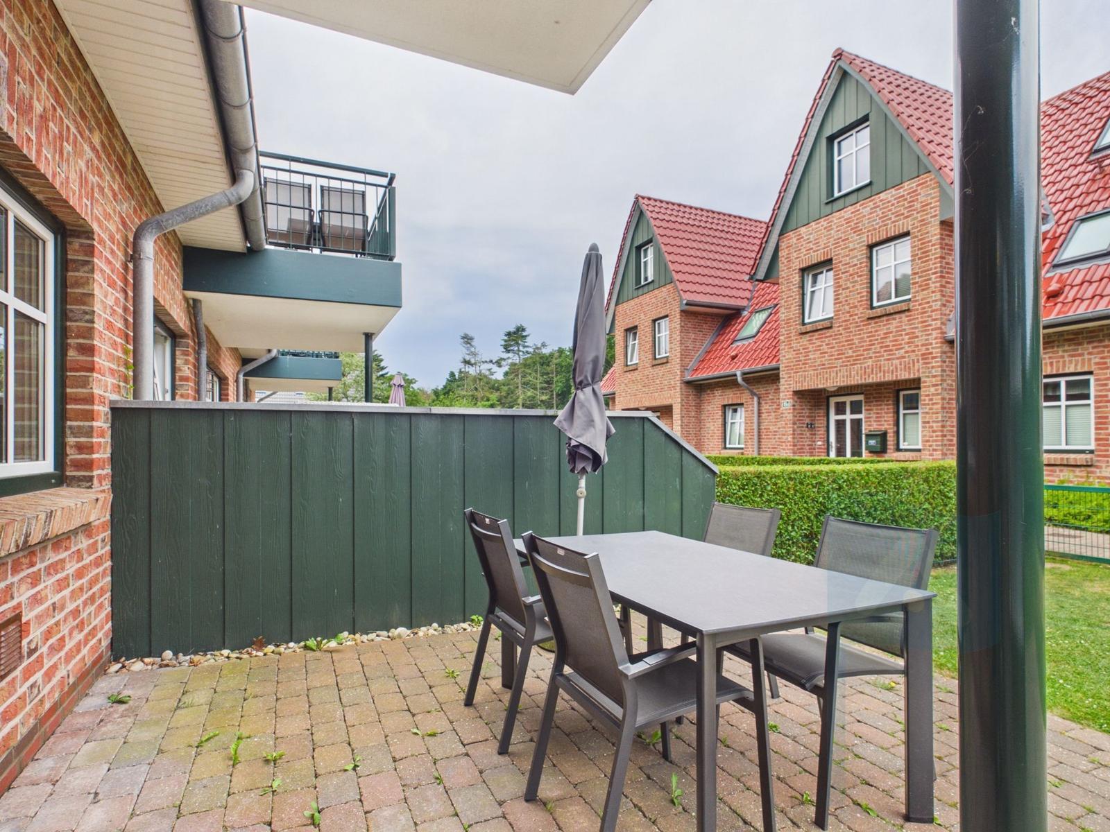 Terrasse mit Tisch und Stühlen, umgeben von grünem Zaun und Wohnhäusern.