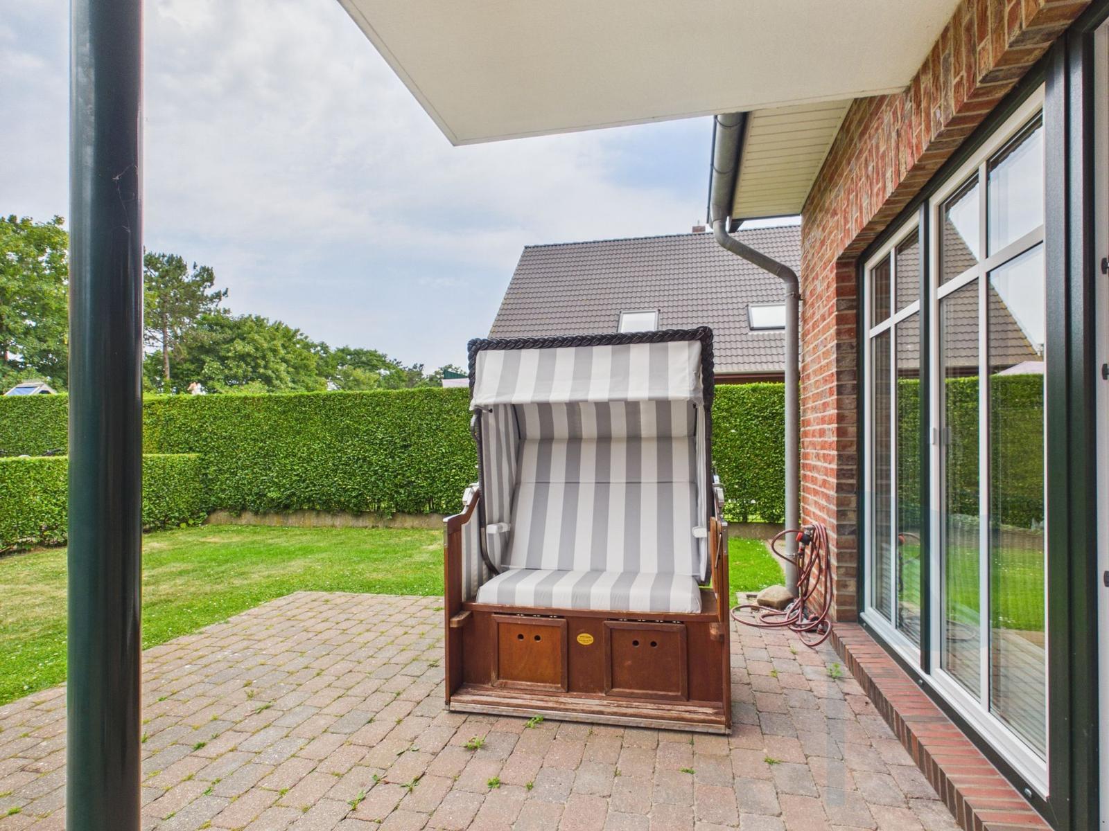 Ein gestreifter Strandkorb steht auf einer Terrasse neben einem Haus mit Fenstern.