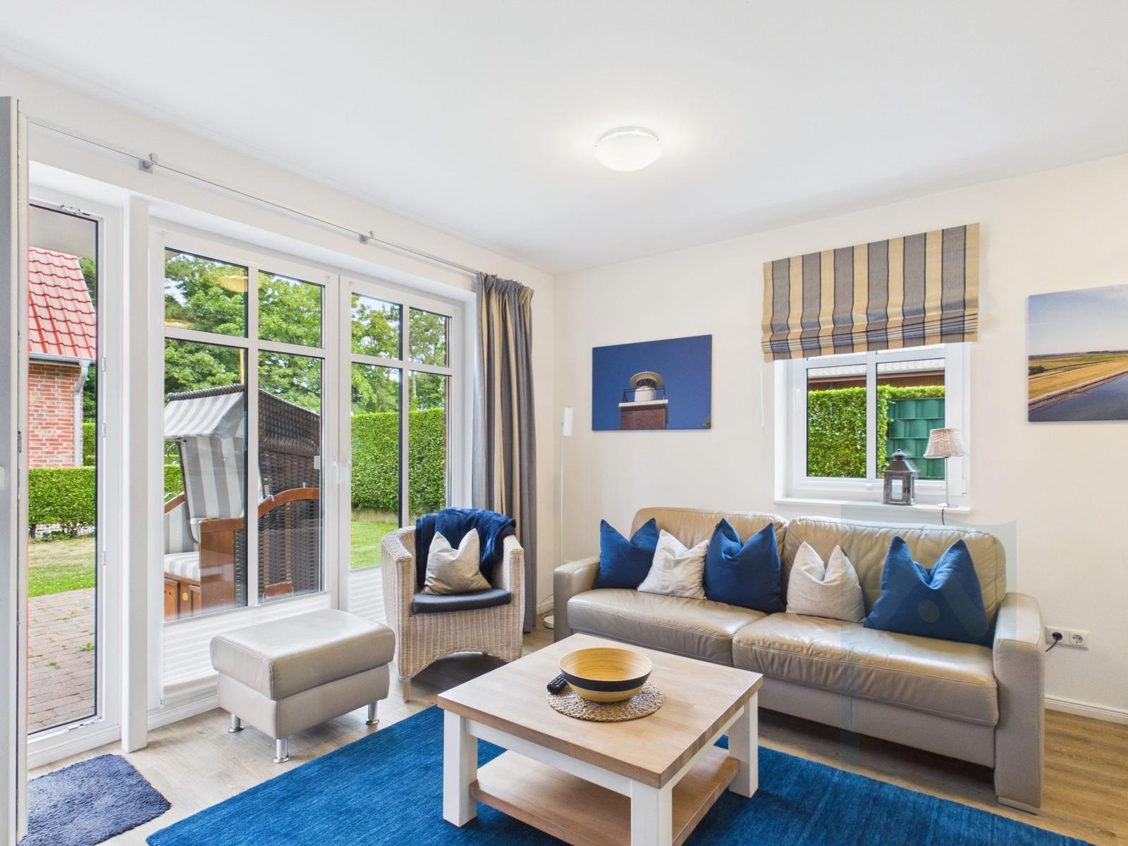 Wohnzimmer mit Sofa, Sessel und Tisch. Große Fenster und Terrasse mit Gartenblick.