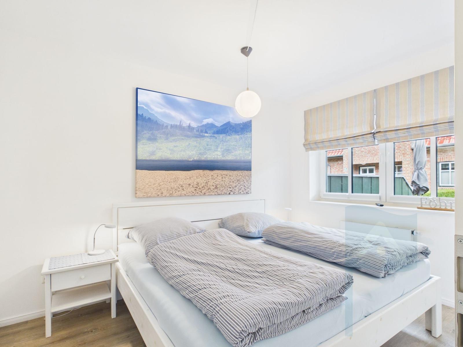 Schlafzimmer mit Bett, Nachttisch und Wandbild. Fenster mit Rollos.