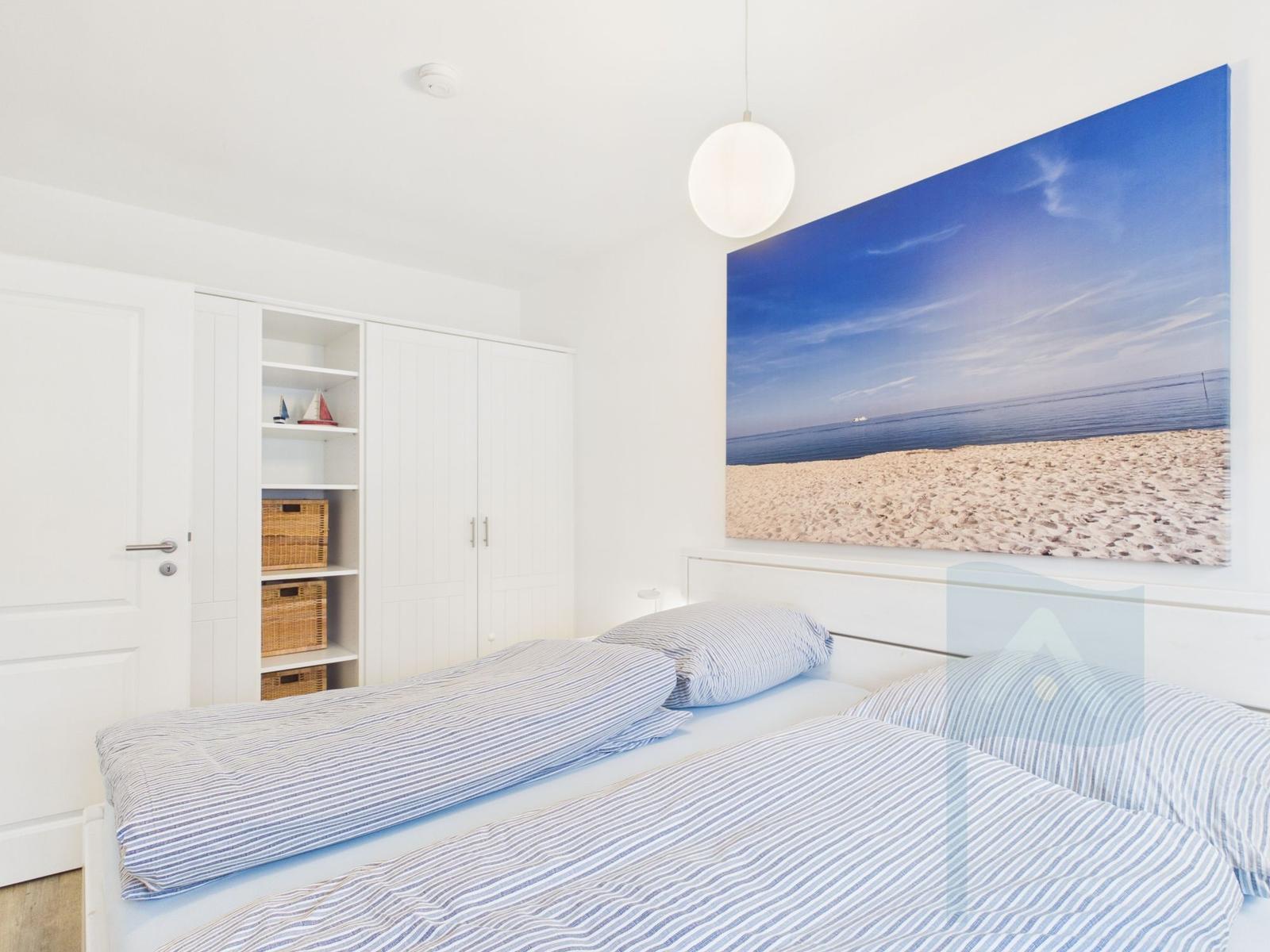 Schlafzimmer mit Bett, Kleiderschrank und Strandbild an der Wand.